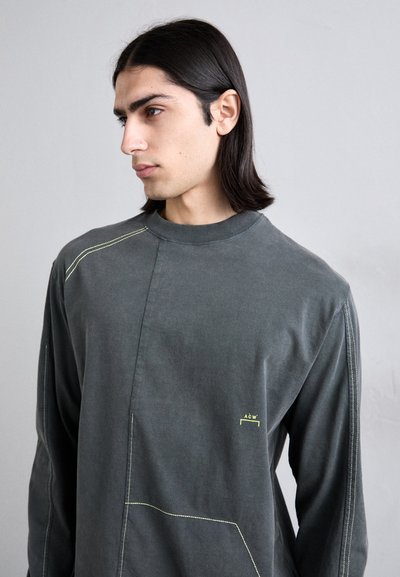 Chemise à manches longues, gris anthracite avec un col haut, dotée de coutures jaunes et d'un détail de poche. Matière en coton douce.