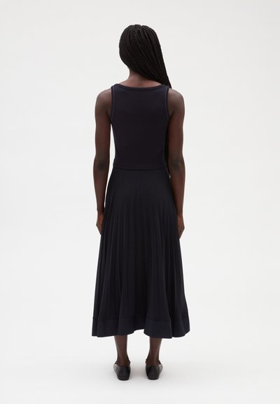 Vestido negro sin mangas con falda plisada, hecho de una tela suave. Corsé estructurado y una falda fluida hasta la rodilla. Detalle de dobladillo simple.