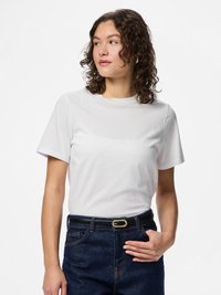 Λευκό κοντομάνικο βαμβακερό μπλουζάκι, φορεμένο με ψηλόμεσα σκούρα μπλε τζιν, με μαύρη ζώνη και χρυσή αγκράφα.