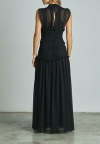 Schwarzes Maxikleid mit einem figurbetonten Oberteil, gerafftem Rücken und transparenten kurzen Ärmeln. Der Rock hat eine fließende Silhouette mit Rüschendetails am Saum.