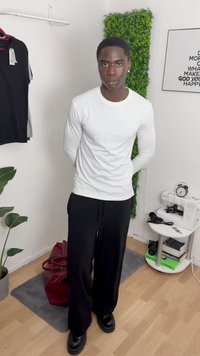 Camicia bianca a maniche lunghe, pantaloni neri a gamba larga e scarpe nere. Design semplice, texture morbida, con una pianta e una borsa sullo sfondo.