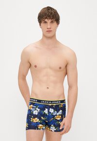 Zilas ziedu apakšveļa ar dzeltenu akcentētu jostu, kurai ir tropisko augu raksti tumšā fonā, izgatavota no viegla auduma.