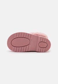 Semelle de botte rose avec motif de grip texturé, bords arrondis et détails de logo. Le matériau semble être en caoutchouc avec une partie supérieure en peluche visible à l'arrière.