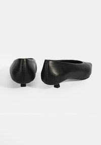 Ballerines noires en cuir avec une finition texturée, bout arrondi et petit talon bloc noir. Design élancé et mince avec une silhouette lisse.