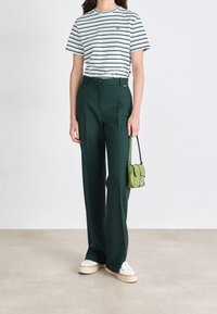 Randig t-shirt i vit, grön och marinblå; högmidjade gröna byxor; liten grön väska; vita sneakers med beige sulor; slätt tyg.