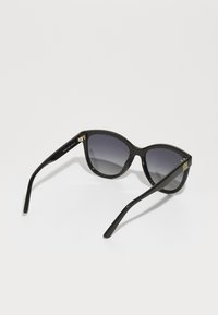 Óculos de sol em forma de gato, estrutura de plástico preto, lentes cinzentas em degradê, detalhe em metal dourado na haste com gravação "AMOR", acabamento brilhante.