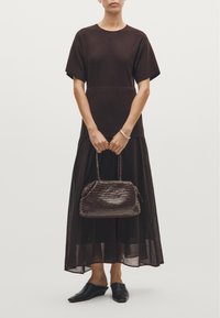 Robe marron à manches courtes avec un bas superposé et transparent. Sac à main tressé de couleur marron foncé avec une forme arrondie. Chaussures noires à enfiler.