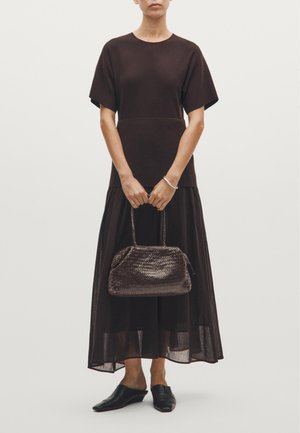 Braunes, kurzärmeliges Kleid mit einem geschichteten, transparenten Unterteil. Geflochtene, dunkelbraune Handtasche in runder Form. Schwarze Slipper.