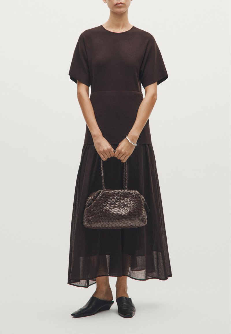 Brun, kortærmet kjole med et lagdelt, gennemsigtigt liggende underdel. Flettet, mørkebrun håndtaske med en rund form. Sorte slip-on sko.