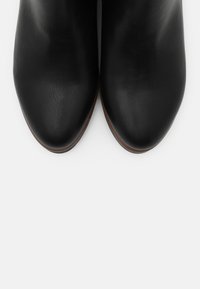 Svarta läderstövletter med slät yta, spetsig tå och platt brun sula. Enkel design utan synliga detaljer eller mönster.