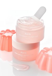 Crema gelatina rosa in un barattolo traslucido con coperchio bianco, con una consistenza liscia. Accompagnata da un applicatore rosa abbinato e uno stampo.