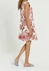 Vit blommig klänning med röda mönster, volangärmar och en svängd nederdel. Matchas med ljuslila sandaletter för en avslappnad look.