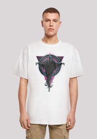 Bílý bavlněný tričko s výrazným grafickým designem postavy s roztaženýma rukama, umístěné na barevném geometrickém pozadí.