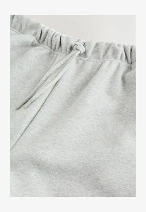 Gaiši pelēkas bikses ar elastīgu jostu un sasienamu aukliņu priekšpusē.