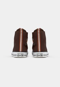 Brązowe, wysokie trampki Converse All Star widziane z tyłu, każda z pionowym czerwono-białym paskiem na pięcie.