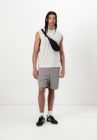 Débardeur gris clair sans manches, short gris, banane noire, baskets noires, chaussettes blanches. Design simple sans motifs remarquables.