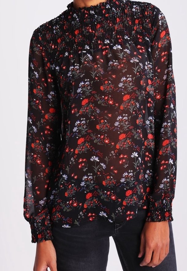 Blouse noire transparente à manches longues avec col et poignets smockés, décorée de motifs floraux rouges et blancs.