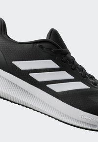 Black athletic shoe with textured fabric upper, white three stripes, and a ridged white midsole. Designed for performance and comfort.