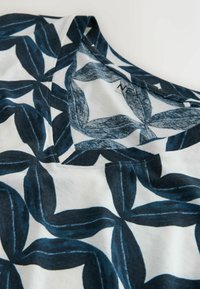 Gros plan sur un tissu blanc avec un grand motif de feuilles bleu foncé et un col en V sur un vêtement décontracté.