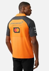 Pomarańczowa i szara koszulka polo zespołu McLaren Formuły 1, z logo z tyłu, z kołnierzykiem i krótkimi rękawami.