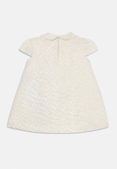 Valkoinen mekko, jossa on teksturoitu, aaltoileva kuvio, lyhyet hihat ja pyöreä kaulus. Kiinnitys takana yhdellä napilla.