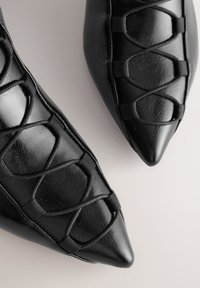 Scarpe nere in pelle con punta appuntita, caratterizzate da una tomaia testurizzata con dettagli intricati a incrocio e inserti elastici per una calzata sicura.