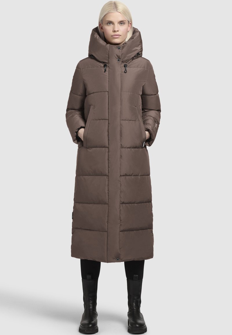 Dolge rjave puhovke z visokim ovratnikom, ki vključuje dve sprednji žep in zategnjenimi kapuco. Gladka tekstura s prešitjem.