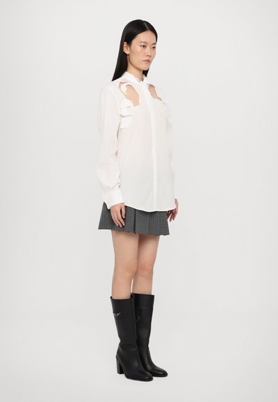 White button-up shirt with cut-out details on shoulders, paired with a gray pleated skirt and knee-high black leather heeled boots.