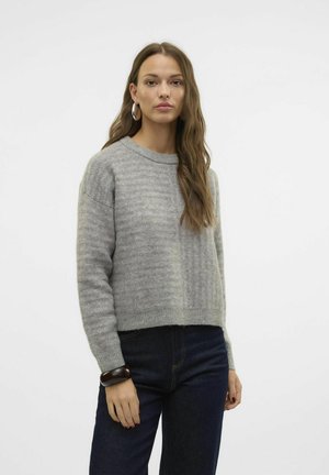 Suéter de punto gris claro con patrón de rayas, escote redondo y hombros caídos, combinado con jeans oscuros y una pulsera gruesa.