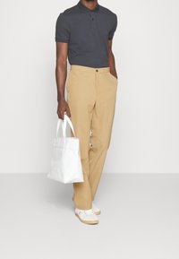 Mörkgrå piké, khakifärgade byxor, vit tote-väska, vita sneakers med ljusa sulor. Pikén har krage; byxorna är rakskurna.