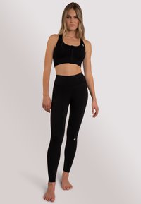 Czarny zestaw treningowy składający się z krótkiego sportowego biustonosza z zamkiem z przodu oraz legginsów o wysokim stanie. Gładka tekstura z detalami logo.