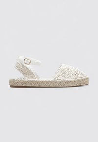 Sandalias de espadrilles blancas con parte superior de tejido trenzado, correa de tobillo ajustable y suela de yute trenzada. Diseño plano con detalles de costura decorativa.