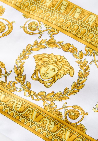 Material alb cu modele galbene complicate, inclusiv cununi de laur și un motiv cu chip, cu margini și detalii ornamentate.