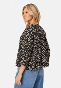 Top a pois nero e beige con scollatura rotonda e maniche a tre quarti, realizzato in tessuto leggero. Abbinato a jeans in denim blu.
