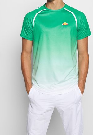 Homme portant un maillot de sport à manches courtes dégradé du vert au blanc avec un petit logo et un short blanc, debout les mains dans les poches.