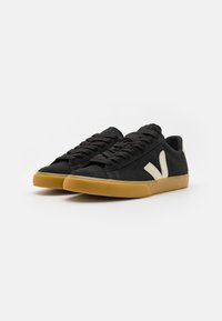 Fekete velúrbőr sneaker gumitalppal. Kiemelkedő bézs logó található az oldalon, lapos fekete fűzőkkel. Lekerekített orr kialakítás.