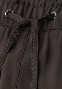 Gros plan sur un tissu marron foncé montrant un cordon noué passant à travers deux œillets métalliques sur une ceinture de vêtement.