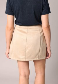 Jupe beige en forme A avec une texture lisse et un léger éclat, dotée d'une couture latérale et d'un ourlet net. Portée avec une chemise à manches courtes bleu foncé.