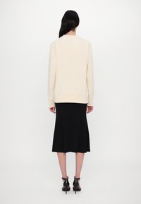 Felpa color crema con maniche lunghe, scollatura rotonda e polsini a costine, indossata sopra una gonna midi nera fluida e scarpe con tacco nero.