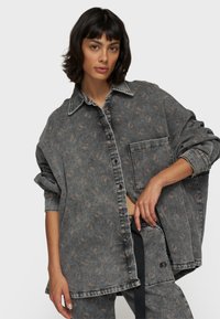 Camicia di jeans grigia oversize con un motivo sottile, chiusura a bottoni sul davanti, taschino sul petto e maniche arrotolate. Tessuto texture con una vestibilità casual.