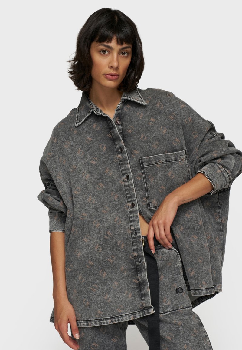 Camicia di jeans grigia oversize con un motivo sottile, chiusura a bottoni sul davanti, taschino sul petto e maniche arrotolate. Tessuto texture con una vestibilità casual.