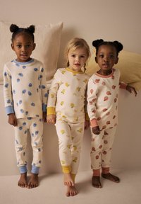 Set van drie kinderpyjama's: crème stof met kleurrijke fruitpatronen, voorzien van blauwe, gele en roze accenten op de manchetten en kragen.