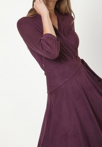 Dunkelviolettes Wickelkleid mit langen Ärmeln, einer Bindegürtellinie und einem glatten, leicht strukturierten Stoff, der einen Überlappungs-Ausschnitt aufweist.