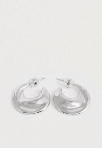 Paari poleeritud hõbedast kuusnurksete rõngaste kõrvarõngaid, selgete plastist tagustega valgel pinnal.