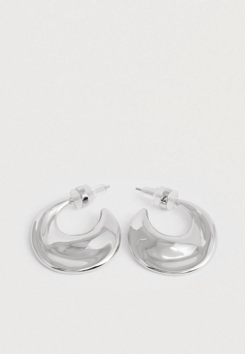 Paari poleeritud hõbedast kuusnurksete rõngaste kõrvarõngaid, selgete plastist tagustega valgel pinnal.