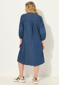 Denim-mekko, jossa on pitkät pallohihat, koristeltu teksturoiduilla brodeerauksilla hihoissa, ja muotoa korostava käännetty takakappale. Yhdistetty rentoihin tennareihin.