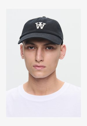 Nuori mies, jolla on päässään musta lippalakki, jossa valkoinen "W"-logo, ja yksivärinen valkoinen pyöreäkauluspaita vaaleaa taustaa vasten.