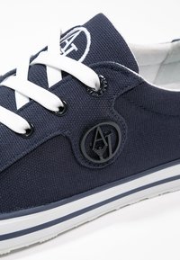 Marineblaue Canvas-Sneaker mit weißen Schnürsenkeln, runden schwarzen Ösen und Logo-Patch an der Seite. Verfügt über eine weiße Gummisohle mit marineblauen Streifen.