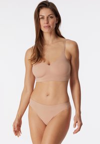 Soutien-gorge sans fil couleur chair avec un design en V et des bretelles réglables, associé à des culottes de bikini sans couture assorties. Texture de tissu lisse.