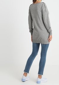 Šedý svetr s dlouhými rukávy a žebrovanými manžetami a spodním lemem. Nosený přes modré skinny džíny a bílé tenisky, s volným střihem a lodičkovým výstřihem.